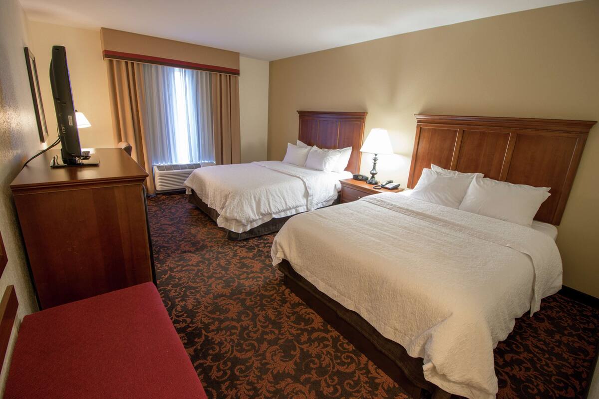 A hotel room with two beds, a desk, a chair, and a television.