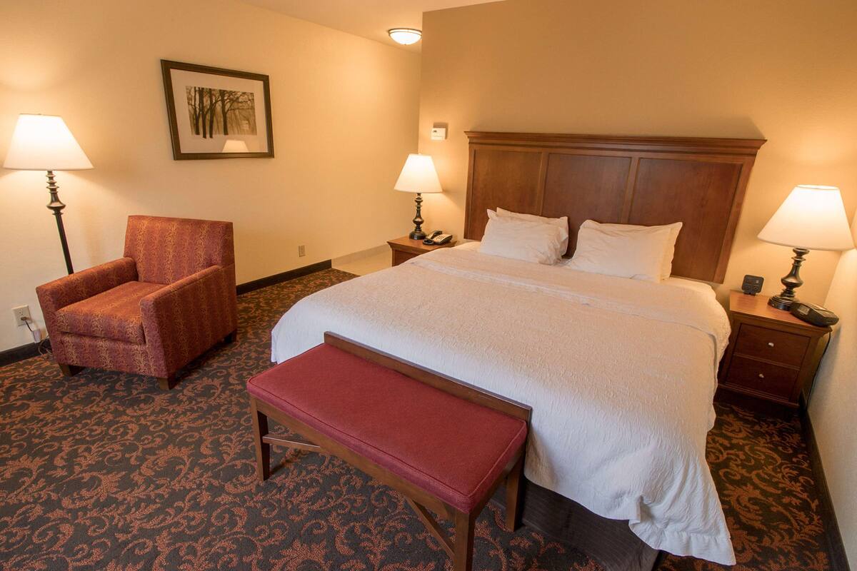 A hotel room with a large bed, two bedside tables with lamps, a chair, and a bench.