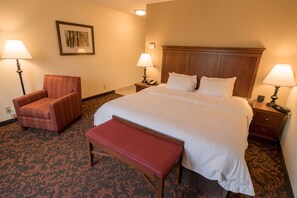 A hotel room with a large bed, two bedside tables with lamps, a chair, and a bench.