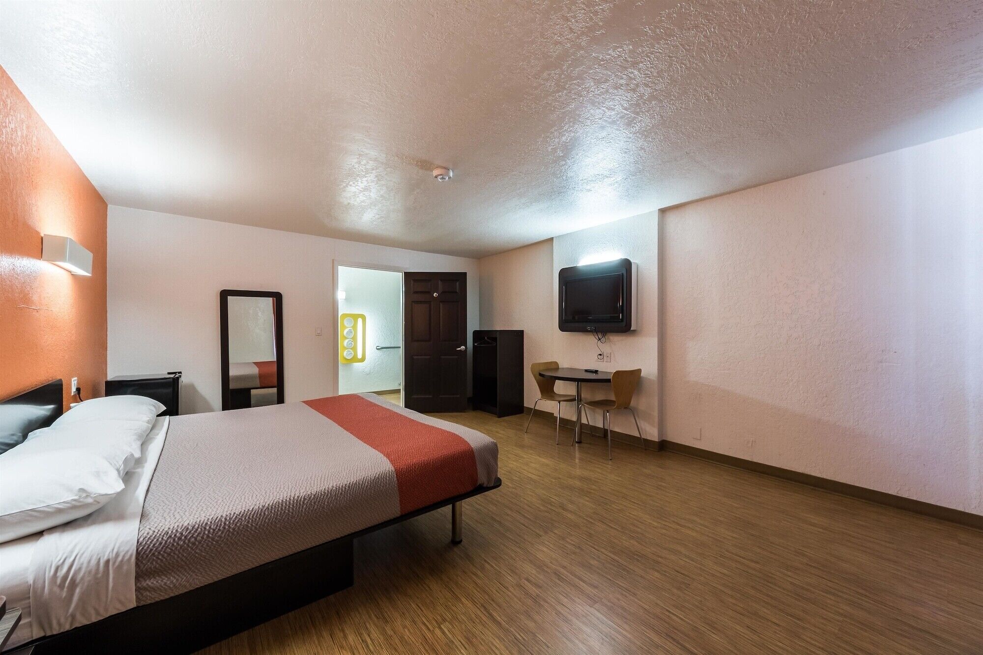 Habitación de hotel con cama, escritorio, silla, televisor y puerta.
