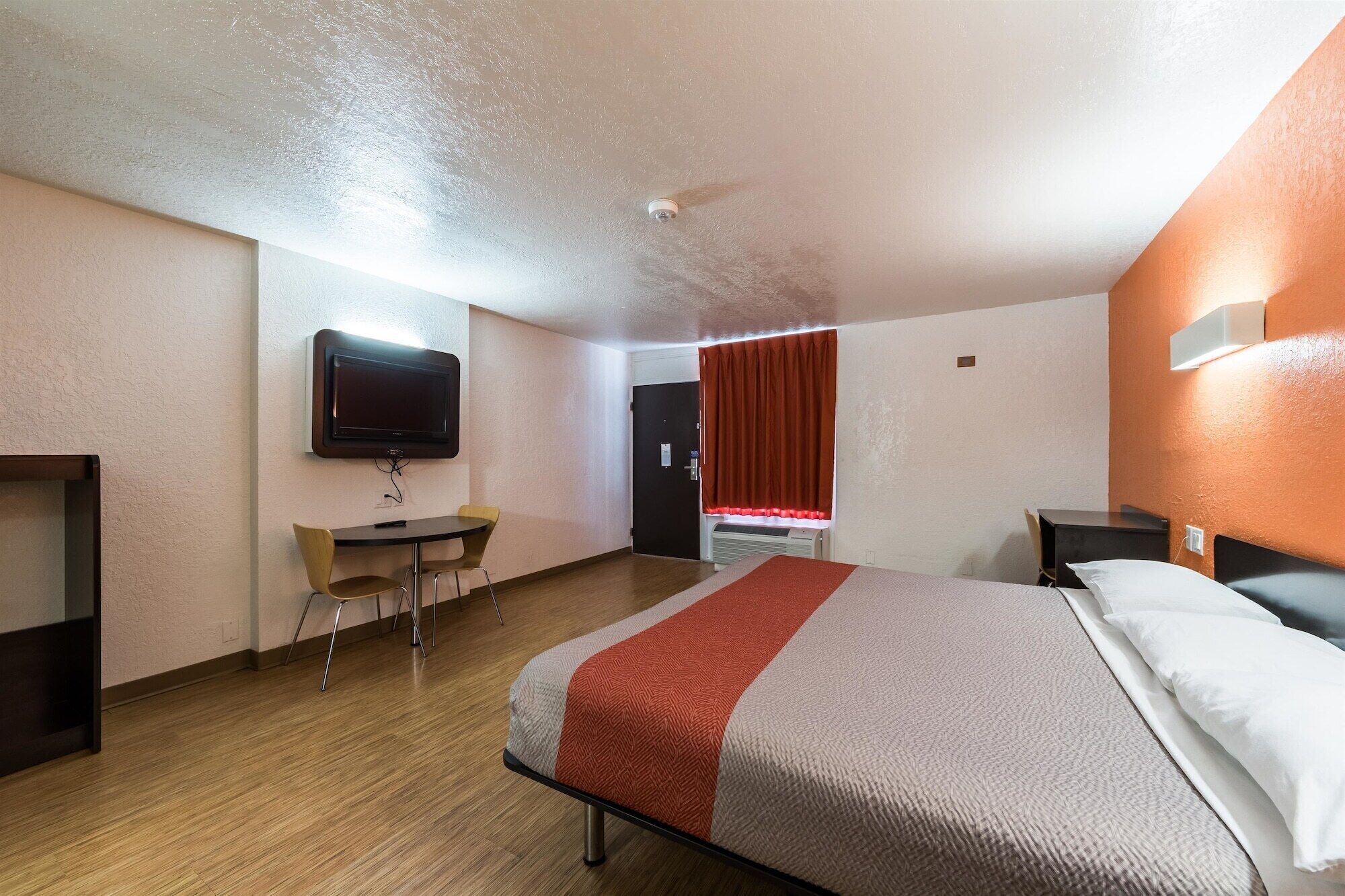 Une chambre d’hôtel avec un lit, un bureau, une chaise, une télévision et une porte.
