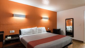 Ein Hotelzimmer mit einer orangefarbenen Akzentwand, einem großen Bett mit weißer und roter Bettwäsche, einem Nachttisch mit Lampe und einem Spiegel an der Wand.
