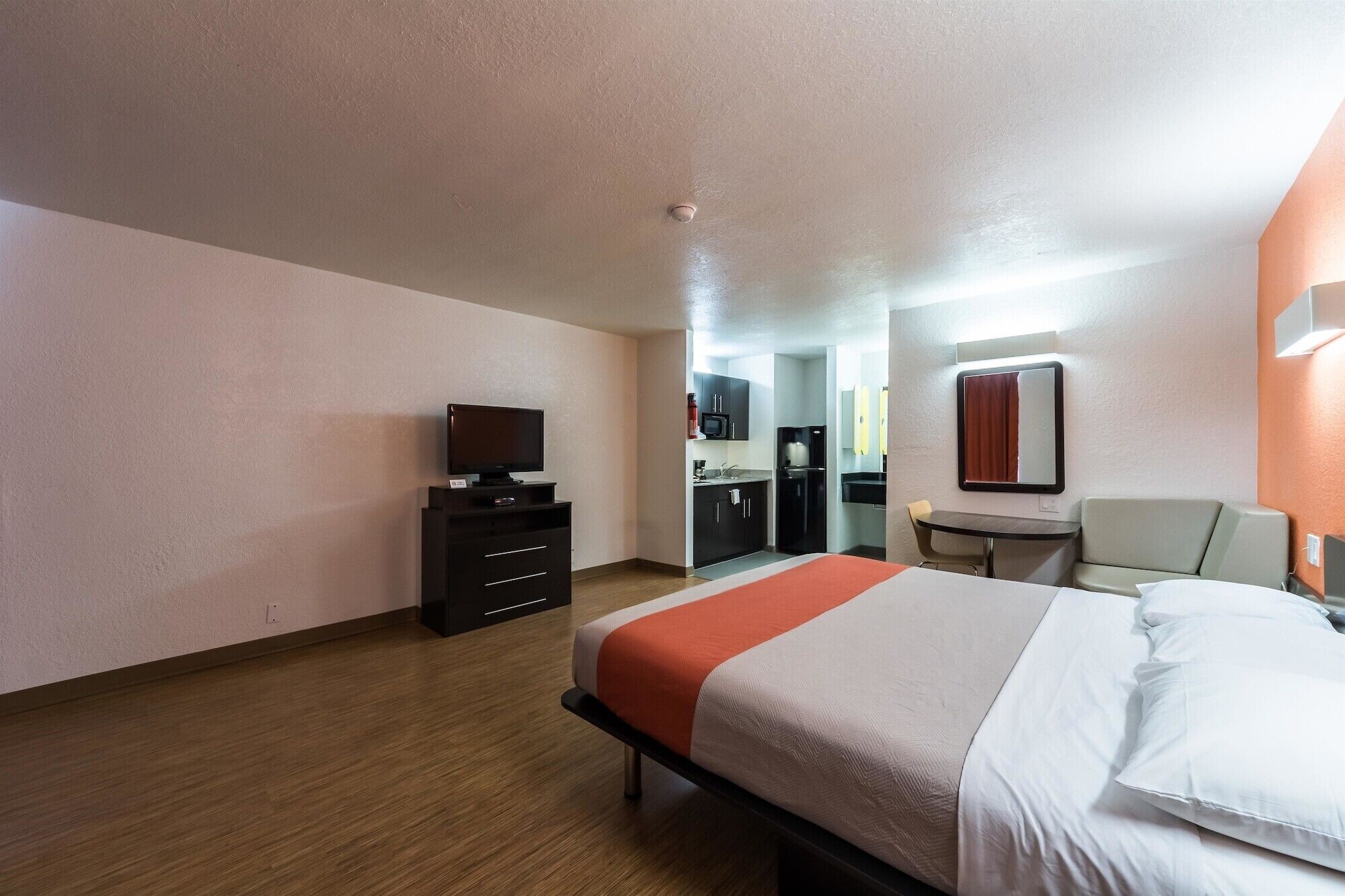 Una habitación de hotel con cama, escritorio, silla, televisión y kitchenette.