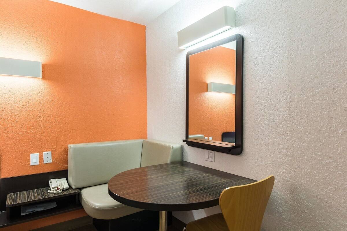 A small, private room with a round table, a single chair, a bench, and a mirror on the wall.