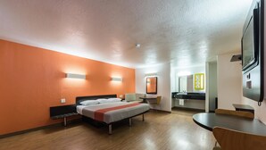 Ein Hotelzimmer mit Bett, Schreibtisch, Stuhl, Spiegel und Fernseher.