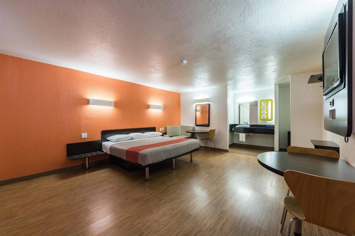 A hotel room with a bed, a desk, a chair, a mirror, and a TV.
