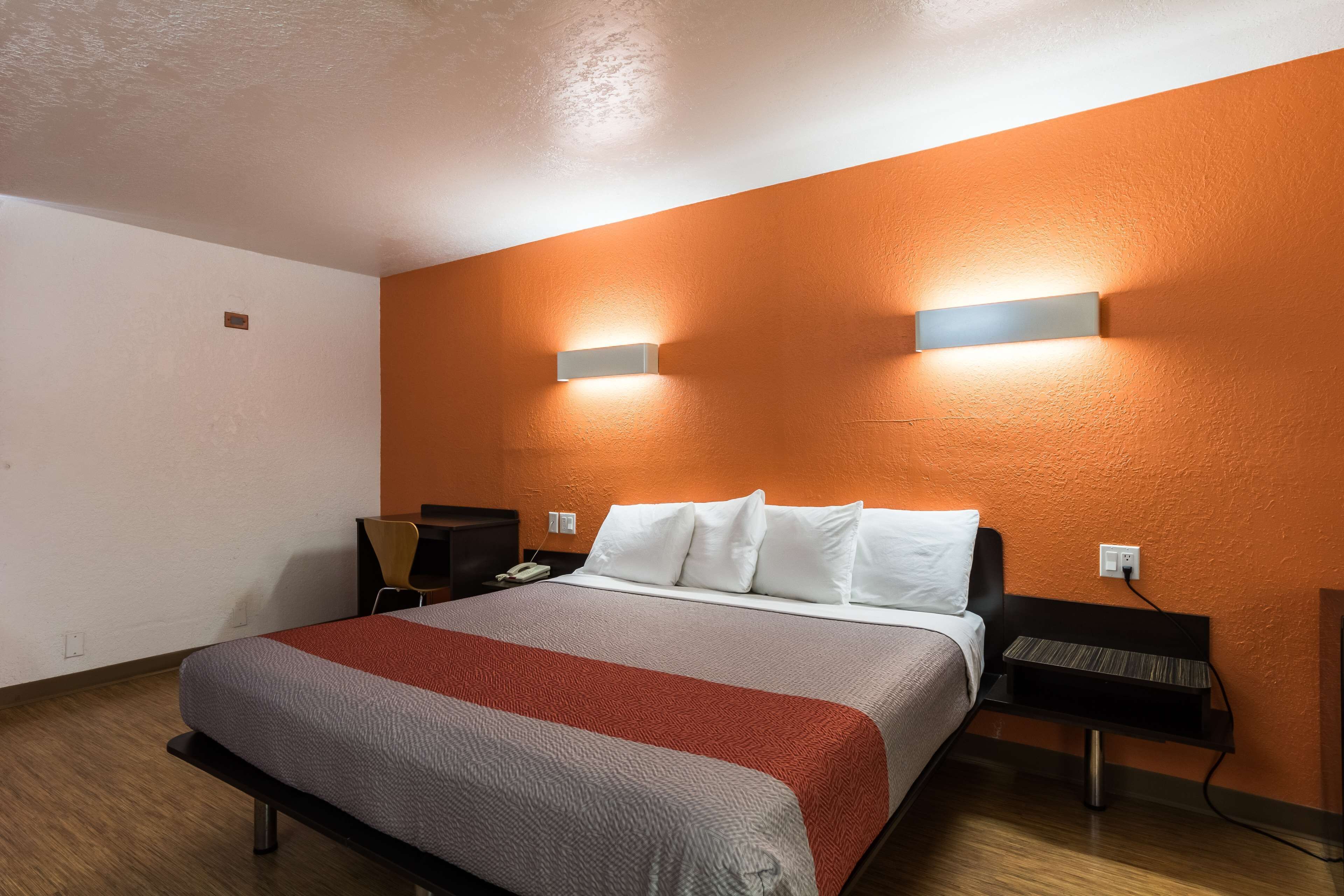 A hotel room with a bed, nightstand, and a desk with a chair.