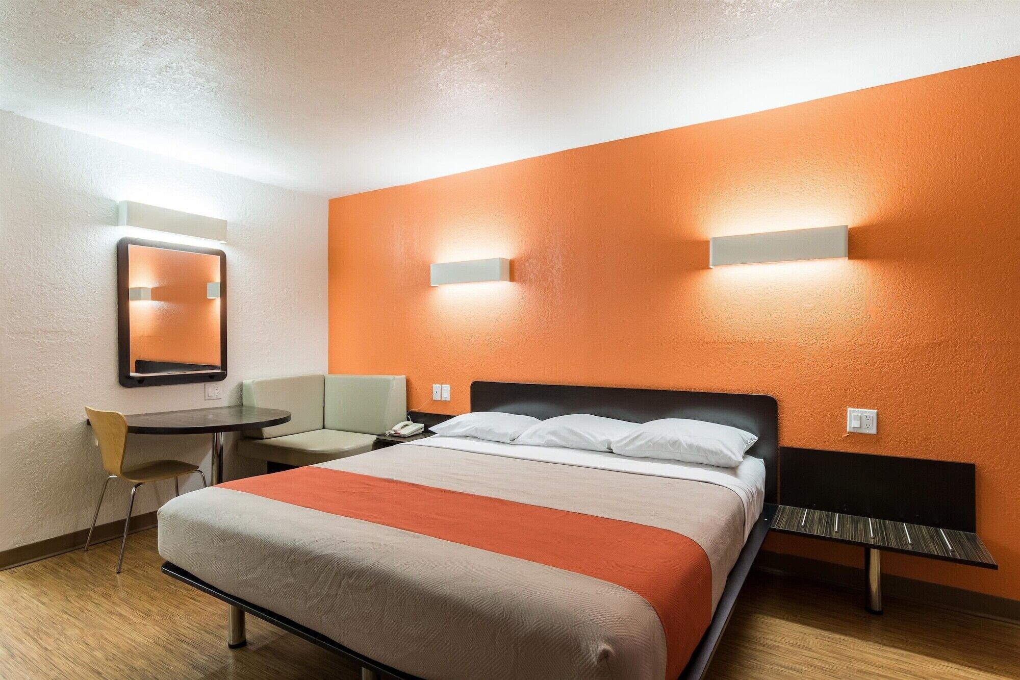 A hotel room with a bed, a desk, a chair, and a mirror.