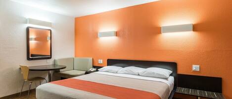 A hotel room with a bed, a desk, a chair, and a mirror.