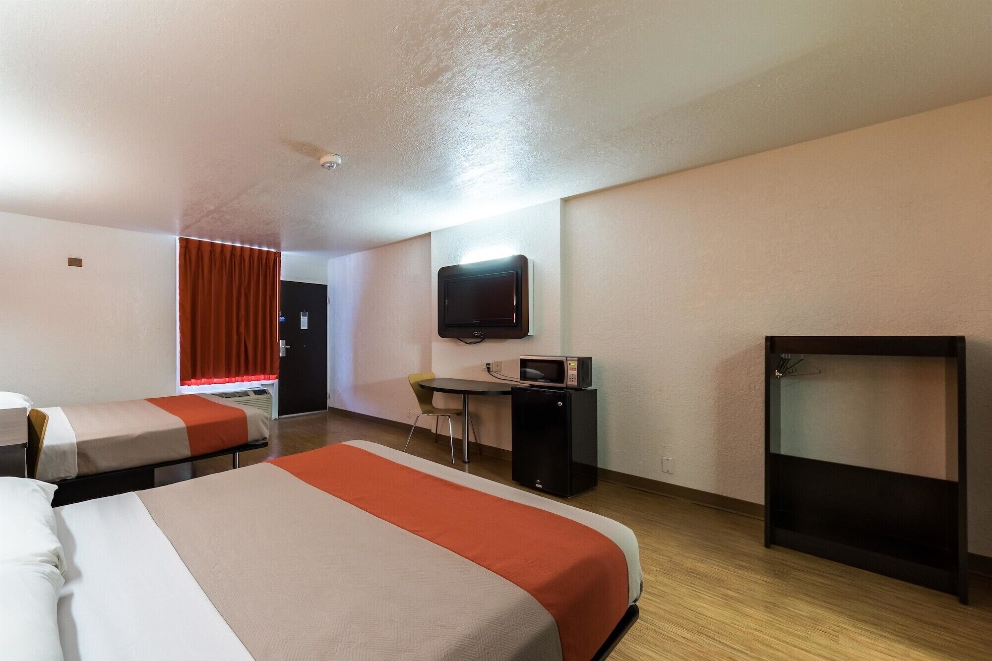 A hotel room with two beds, a desk, a television, and a small kitchenette.