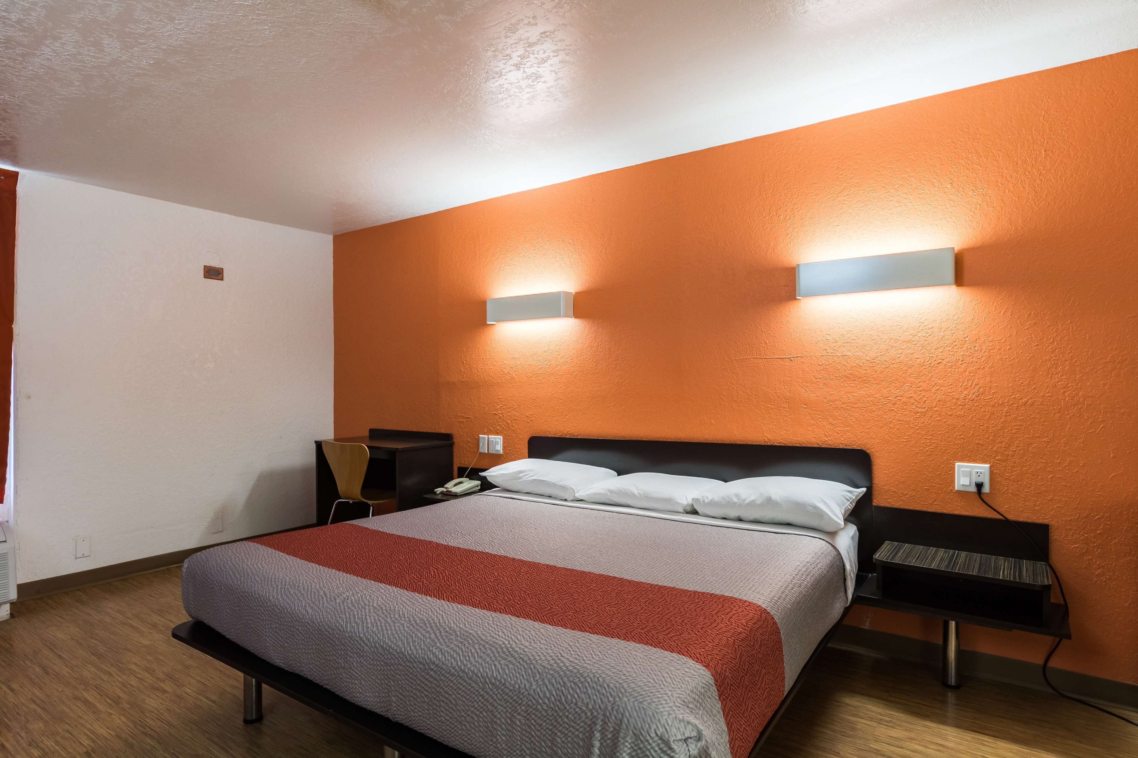 A hotel room with a large bed, two bedside tables, a nightstand, and a wall-mounted light fixture.