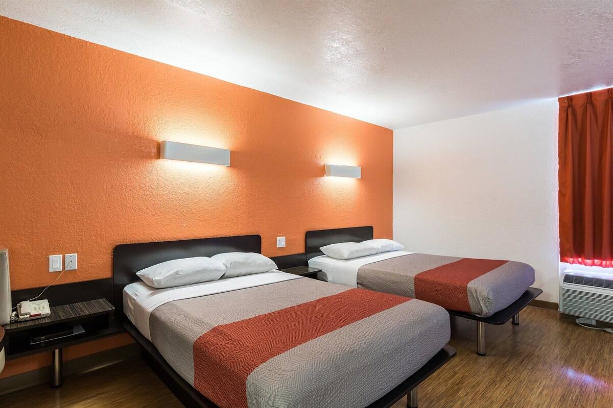 A hotel room with two beds, a wooden floor, and a red curtain.