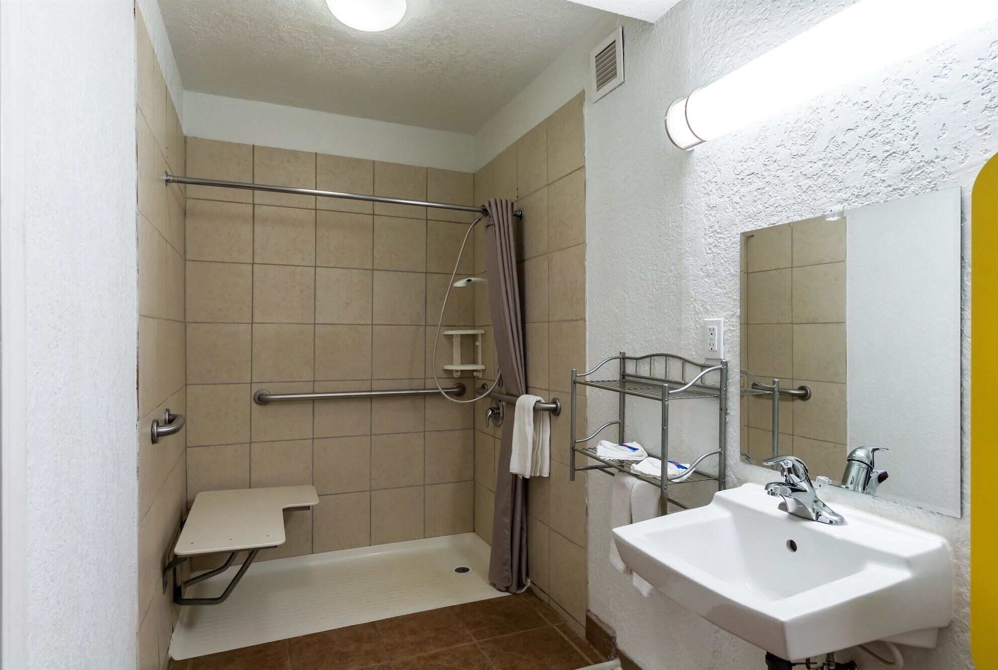 A small, single-room bathroom with a shower, a sink, and a mirror.