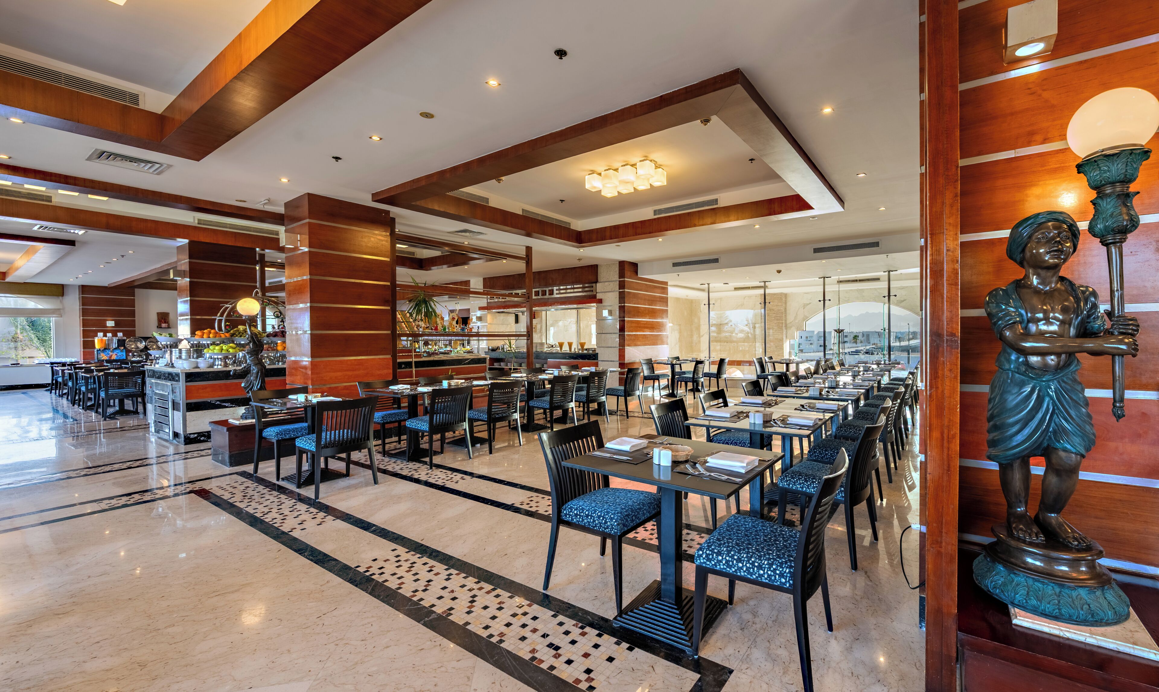 A spacious hotel lobby with a long dining area, a reception desk, and a statue.