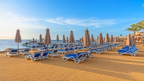 A beach with rows of sun loungers and umbrellas, a pier extending into the water, and a clear sky. - Xperience Sea Breeze Resort (Sharm El Sheikh)