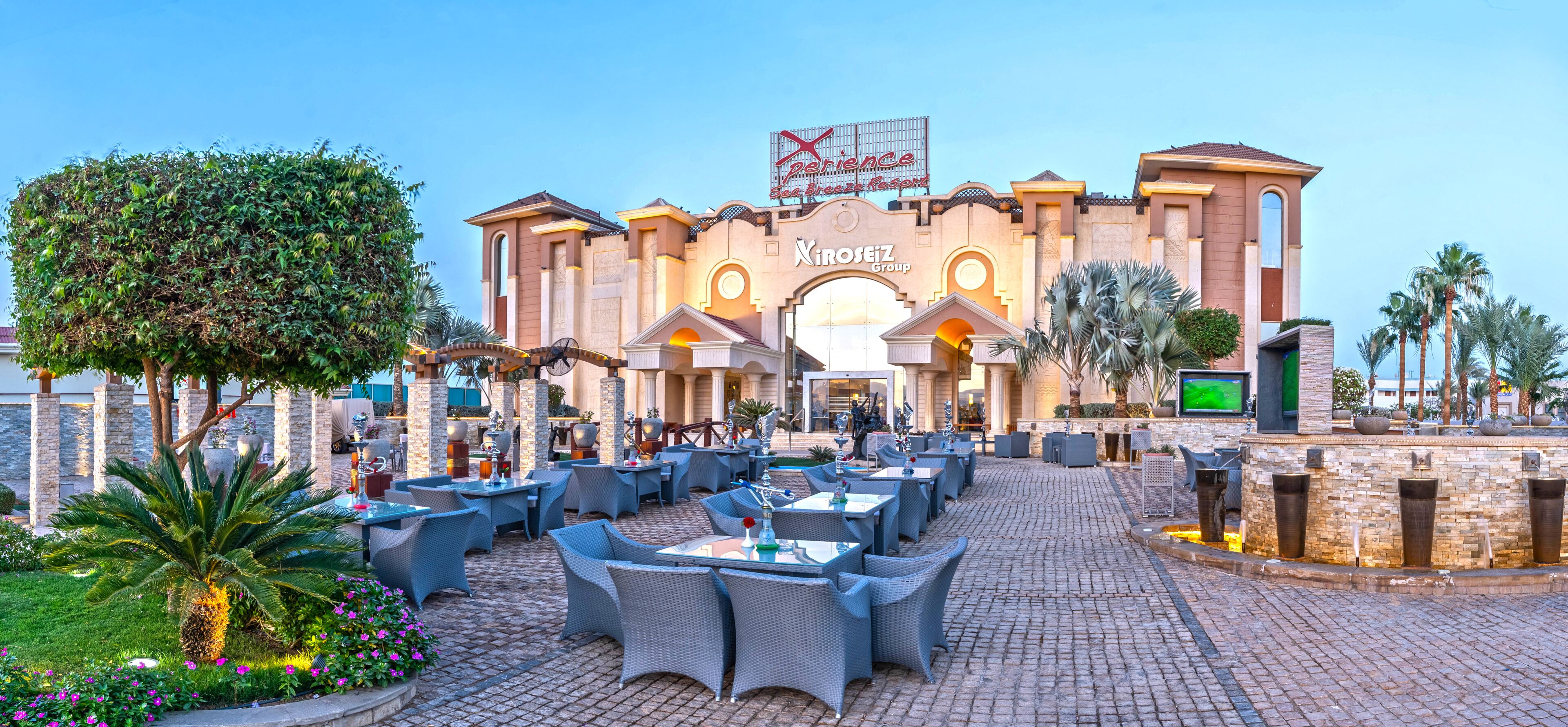 A hotel entrance with a large archway, outdoor seating area, and palm trees.