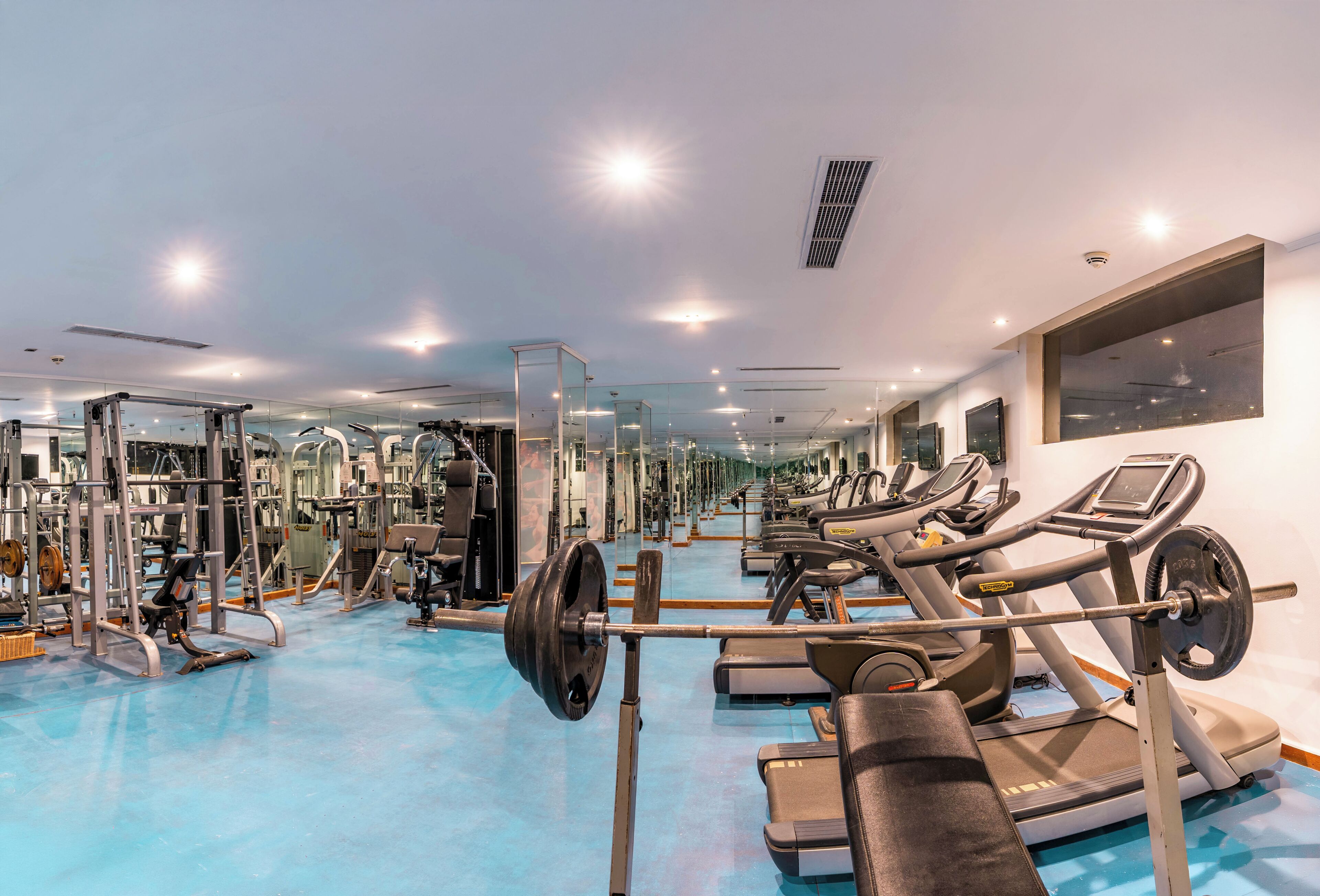 Ein Fitnessstudio mit Trainingsgeräten, Spiegeln und einem blauen Boden.
