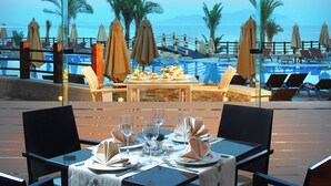 A dining area with a table set for two, overlooking a pool and palm trees. - Xperience Sea Breeze Resort (Sharm El Sheikh)