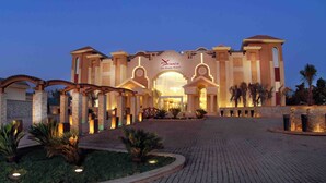 A hotel entrance with a grand archway, a well-lit facade, and a landscaped driveway. - Xperience Sea Breeze Resort (Sharm El Sheikh)