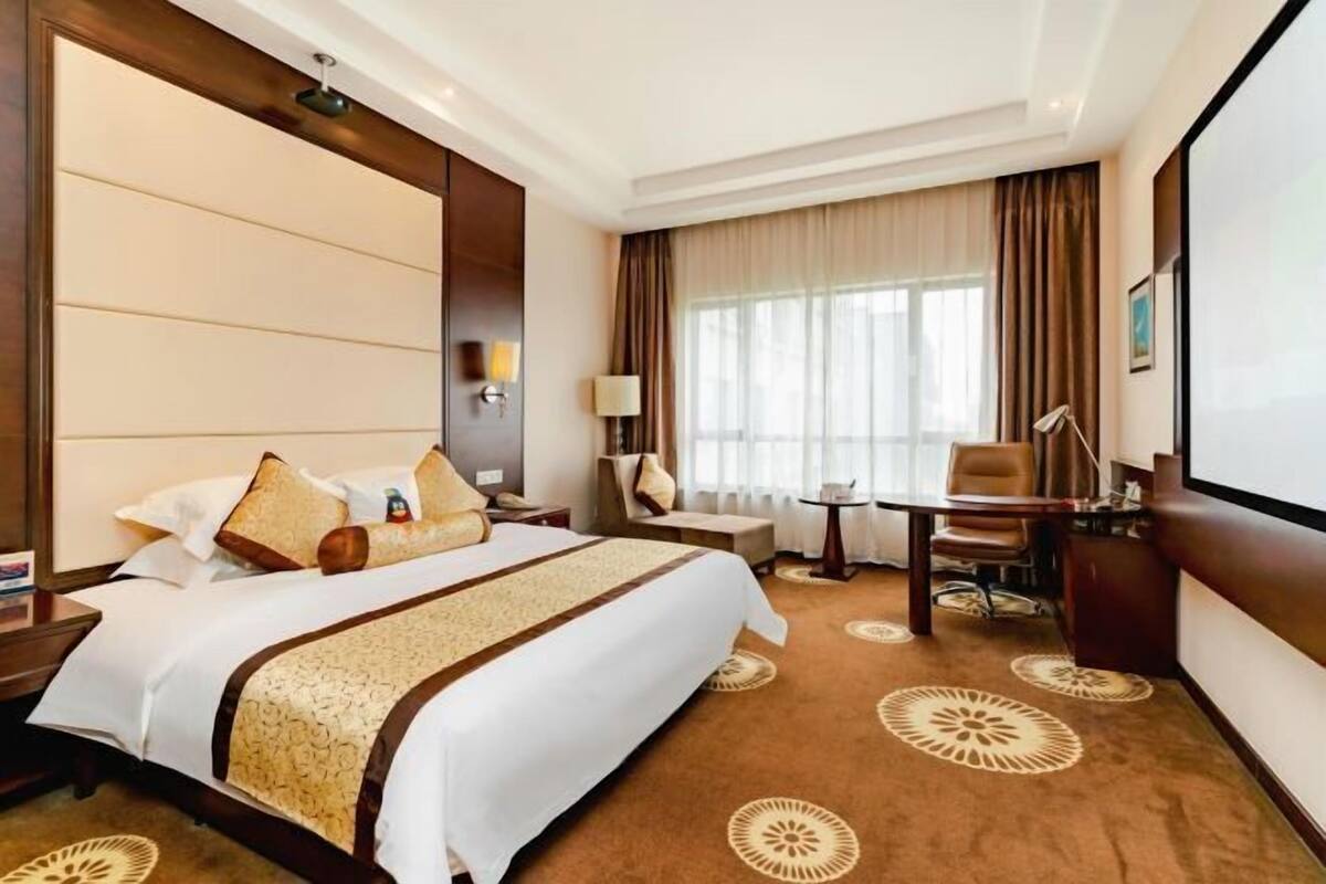Una habitación de hotel con una cama grande, un escritorio, una silla, una lámpara y un televisor.