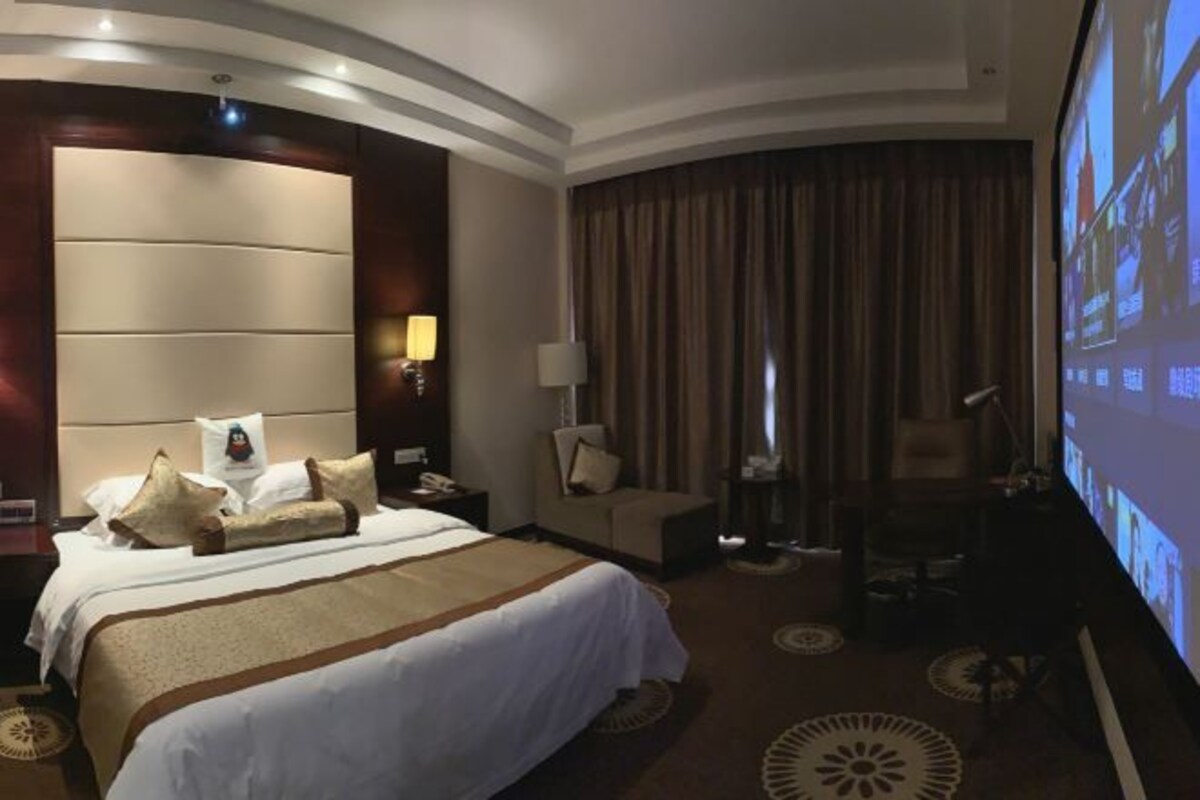 Habitación de hotel con una cama grande, un escritorio, una silla, un televisor y un ventanal con cortinas.