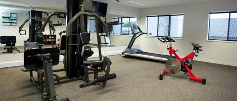 Ein Fitnessstudio mit Cardiogeräten, Gewichten und einem roten Hantelrad.
