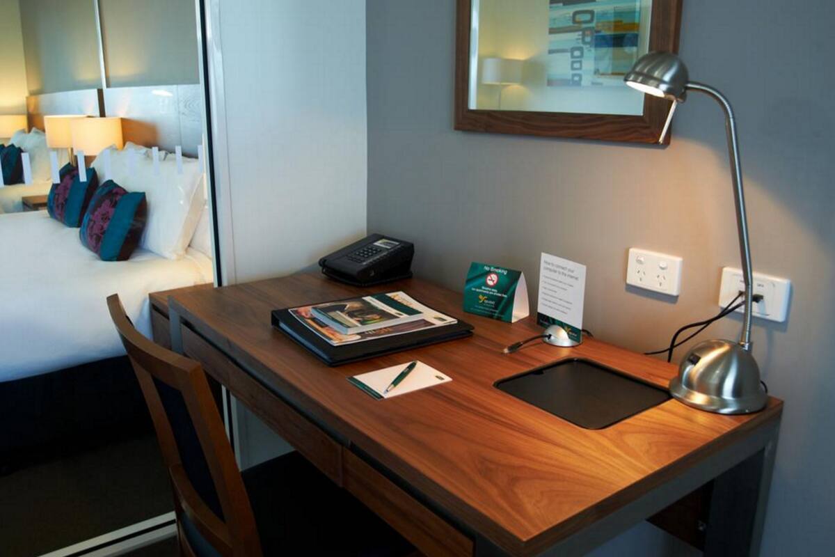 A hotel room desk with a laptop, a tablet, a telephone, a desk lamp, and a small sign.