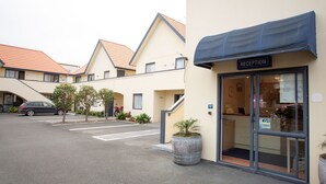 A reception area with a blue awning, a car parked in the lot, and a building with a red-tiled roof. - Bella Vista Motel New Plymouth (New Plymouth)