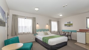 A hotel room with a bed, a desk, a chair, and a small kitchenette. - Bella Vista Motel New Plymouth (New Plymouth)