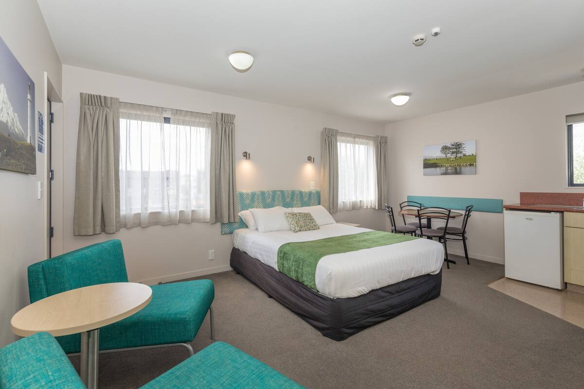 A hotel room with a bed, a desk, a chair, and a small kitchenette.