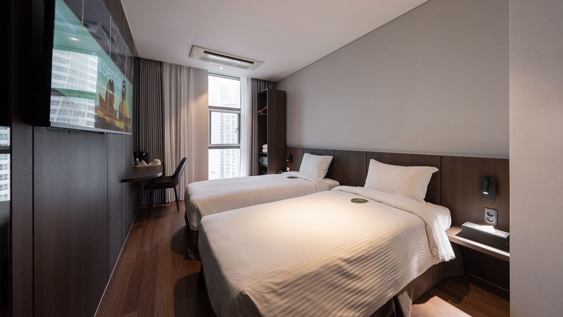 Ein Hotelzimmer mit zwei Betten, einem Schreibtisch, einem Sessel, einem Fernseher und einem Fenster mit Vorhängen.