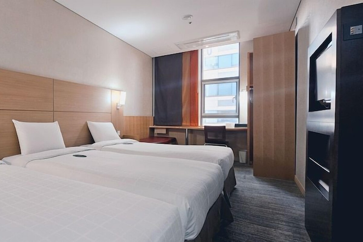 Habitació d'hotel amb tres llits, un escriptori, una cadira i una televisió.