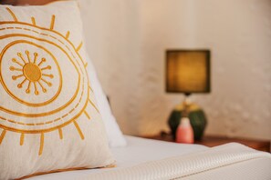 A bed with a pillow featuring a sun design, a bedside table with a lamp, and a vase with flowers.