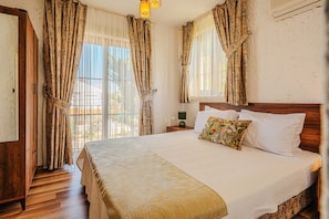 A bedroom with a large bed, wooden headboard, curtains, a nightstand, and a lamp.