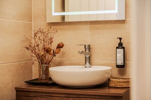 A bathroom with a white sink, a mirror above it, and a bottle of soap on the wall.