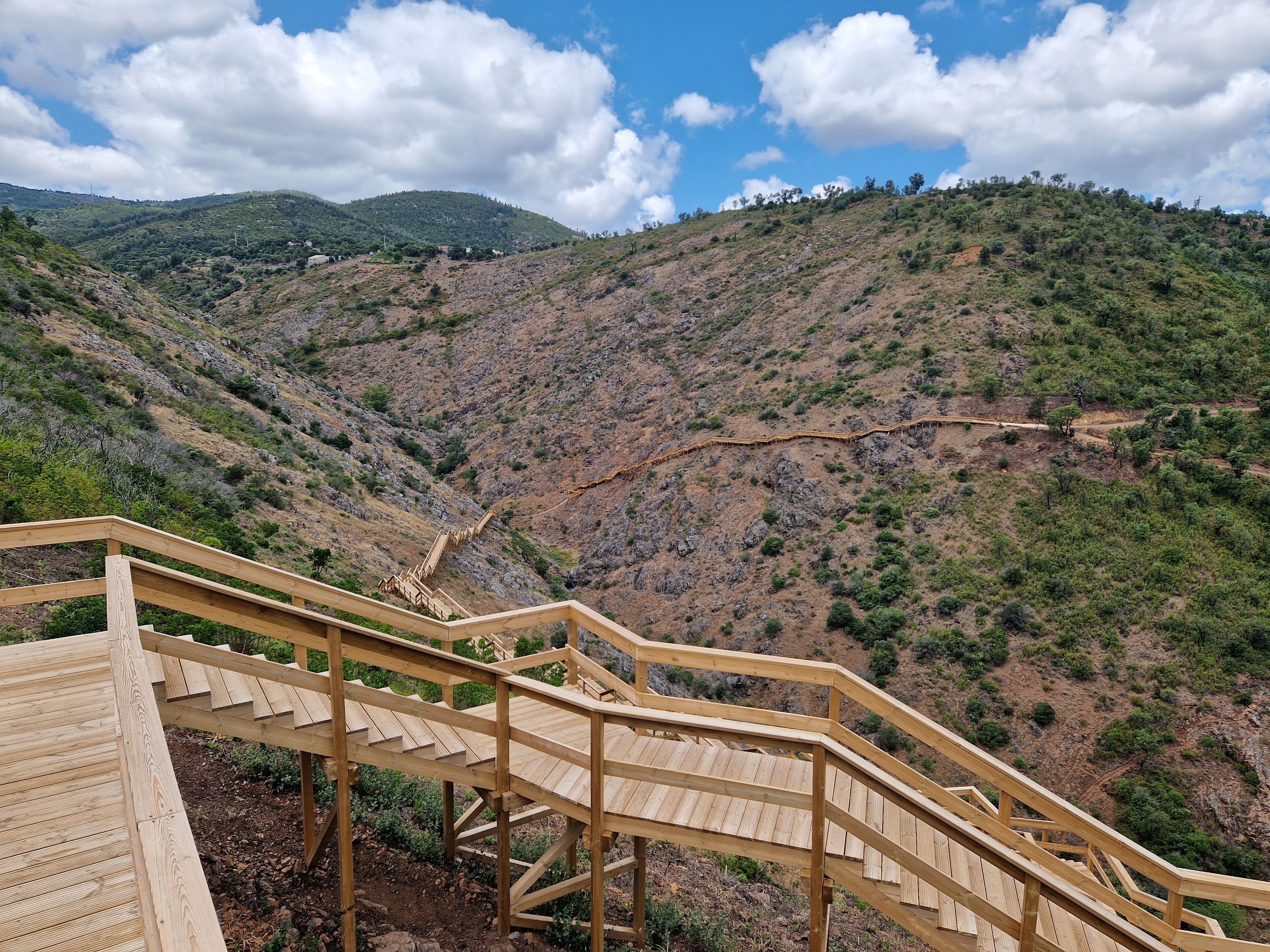 A wooden staircase leading up a hillside with a view of a valley and distant mountains.