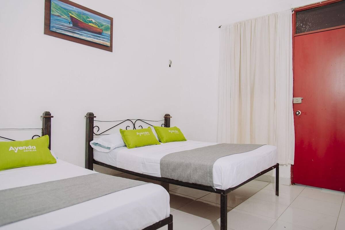 Une chambre d’hôtel avec deux lits, chacun doté d’un matelas blanc et d’oreillers verts, une porte rouge et un tableau accroché au mur.