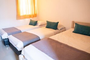 A hotel room with three single beds, each with a pillow and a blanket.