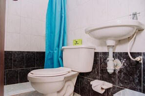 A bathroom with a toilet, a blue shower curtain, a sink, and a marble-tiled wall.