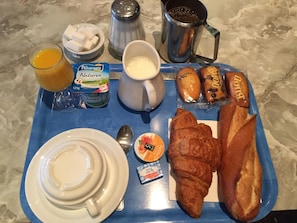 Ein Frühstücksbrett mit Croissants, Gebäck, Orangensaft, Kaffee, Zuckerwürfeln und Beilagen.