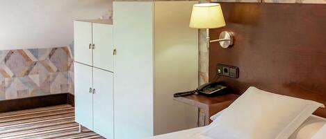 Una habitación de hotel con una cama, una mesita de noche con una lámpara, un teléfono y un armario.