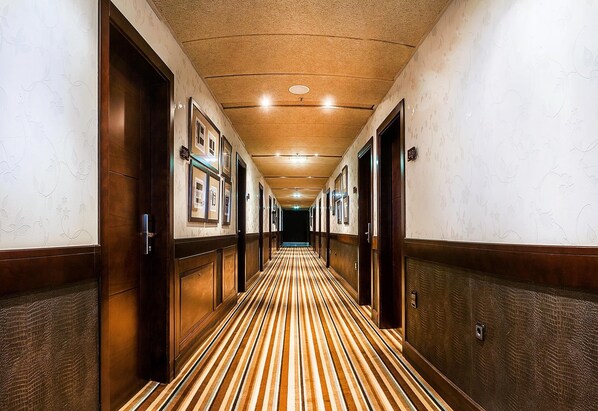 Un couloir d’hôtel avec des portes en bois, des tableaux encadrés et un tapis à rayures.