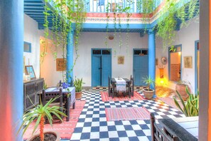 A courtyard with a checkered floor, blue doors, and hanging plants. - Les Matins Bleus (Essaouira)