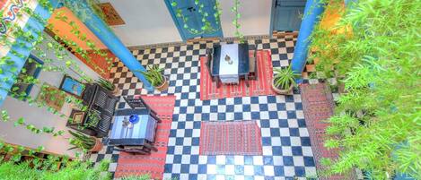 A courtyard with checkered flooring, a central table with chairs, and potted plants.