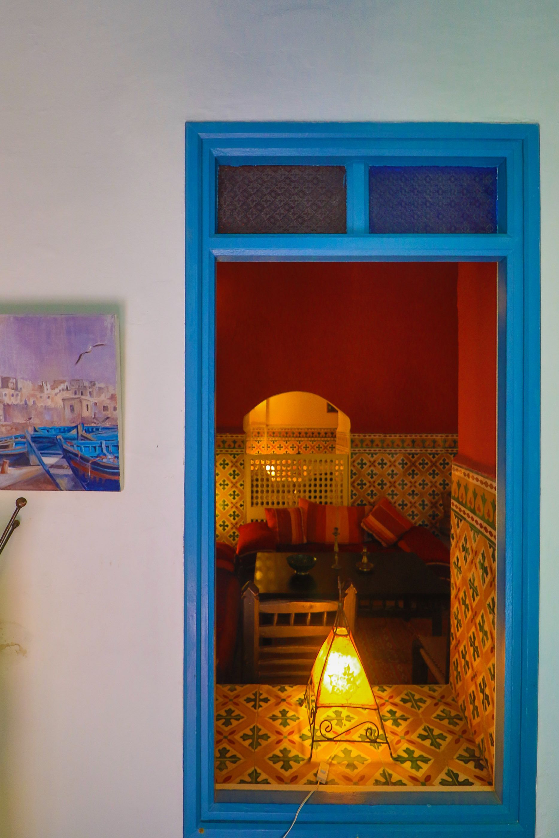 A room with a blue-framed window, a patterned floor, and a red wall.