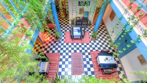 An indoor courtyard with checkered flooring, potted plants, and a central seating area. - Les Matins Bleus (Essaouira)