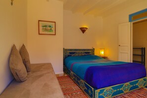 A bedroom with a bed, a sofa, a framed picture on the wall, and a wall-mounted light fixture. - Les Matins Bleus (Essaouira)