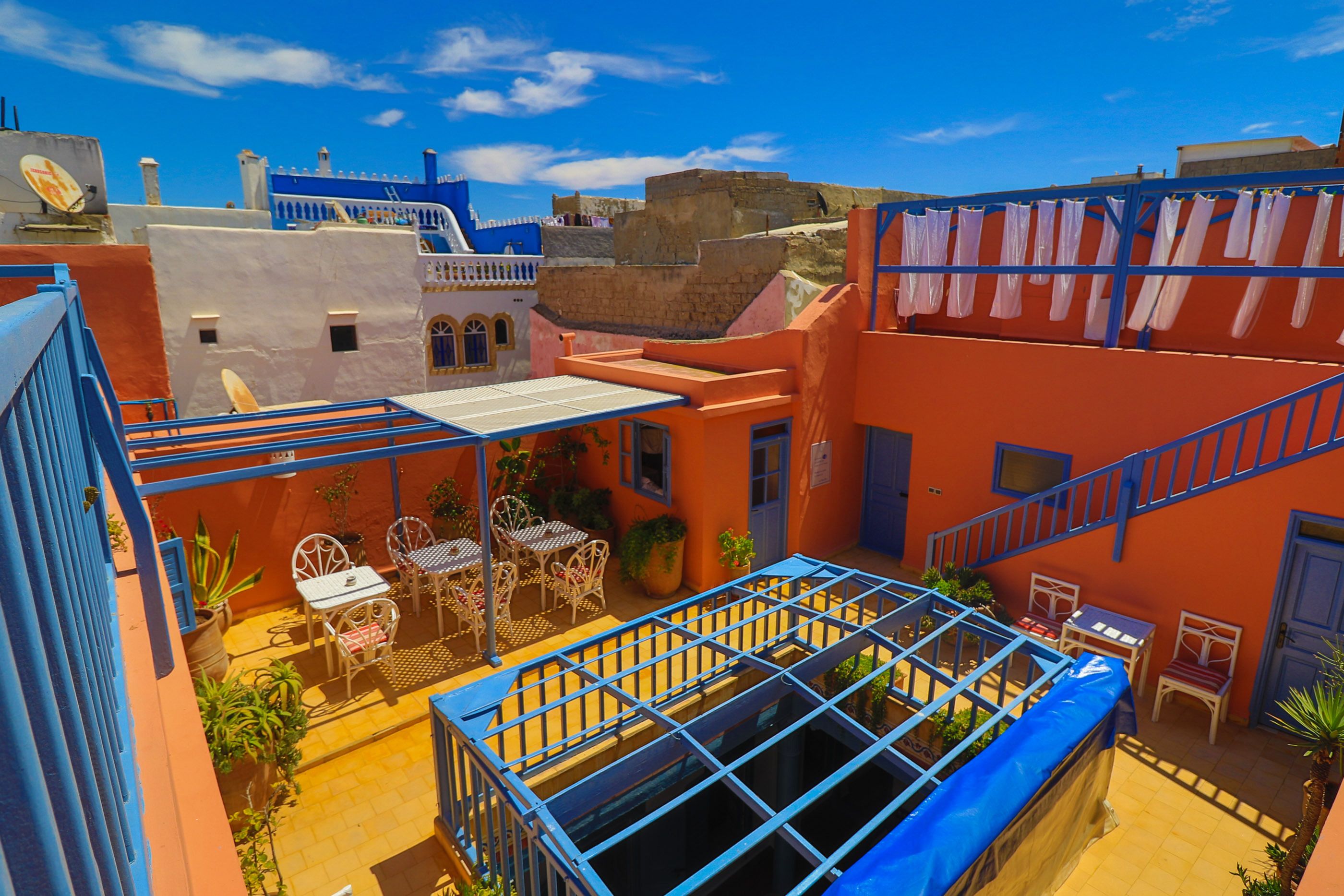 A rooftop terrace with a blue metal railing, outdoor seating, and a view of the surrounding buildings.