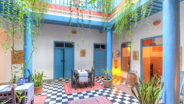 A courtyard with checkered flooring, blue doors, hanging plants, and a table with chairs. - Les Matins Bleus (Essaouira)