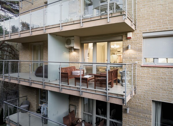 A multi-story apartment with a balcony, furnished with a sofa, chairs, and a dining table.